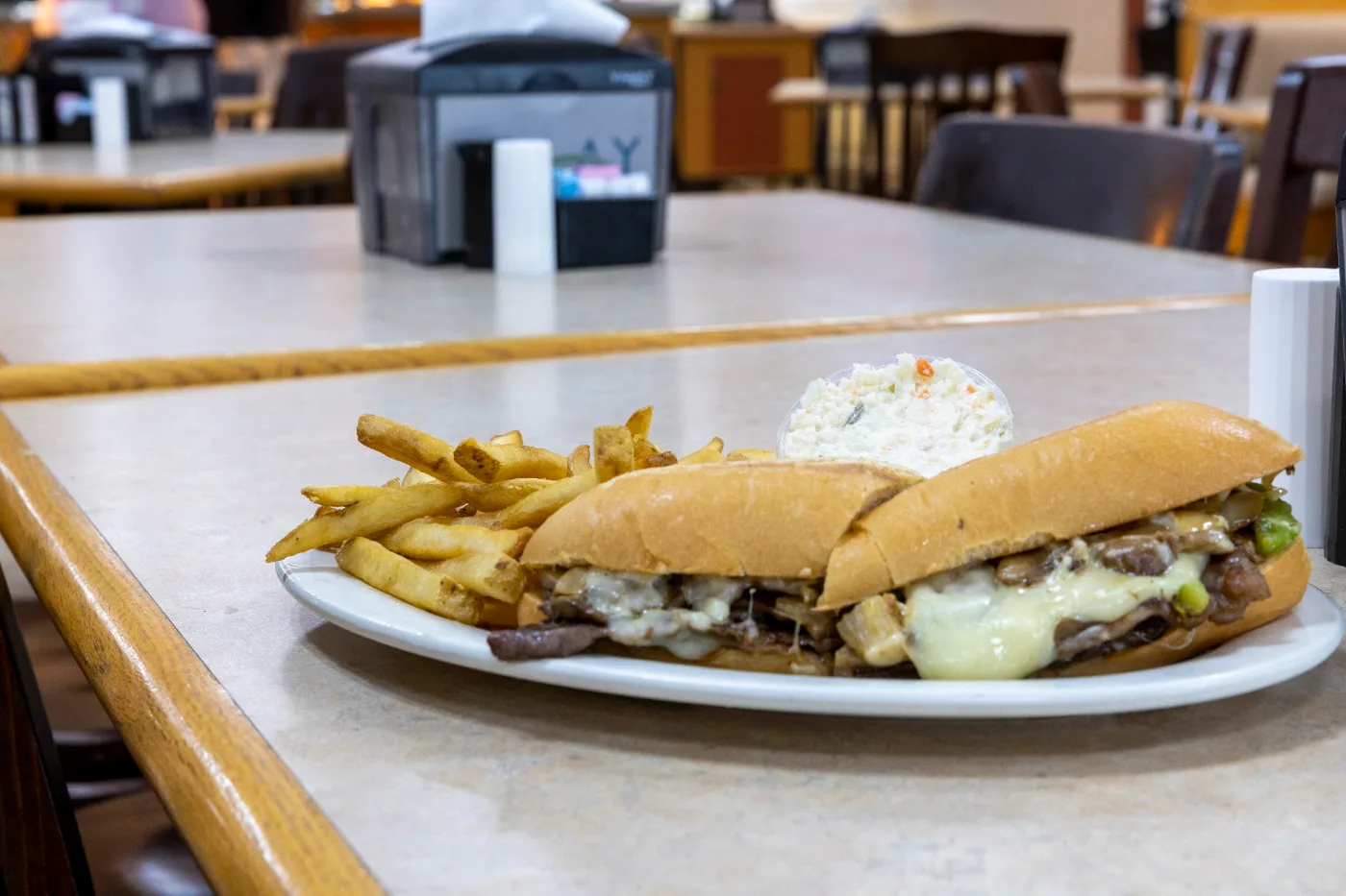 Philly cheesesteak sub with melted cheese, fries, and a side of coleslaw